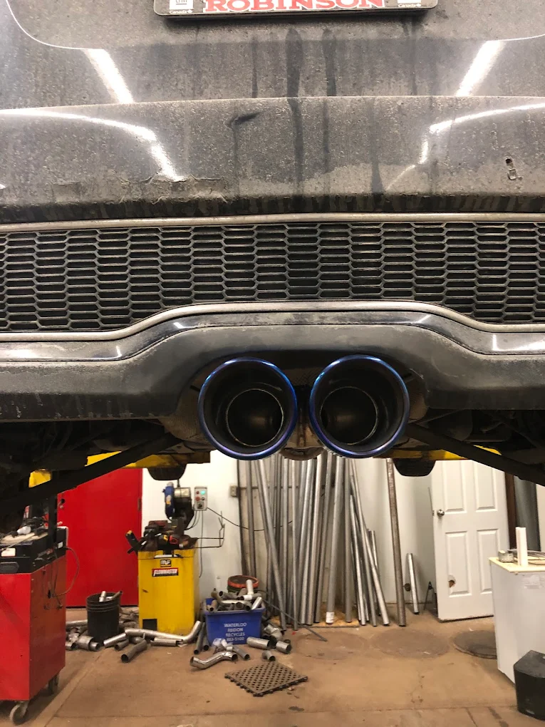 Blue-tipped twin exhaust outlets with racks of exhaust pipe stock visible behind